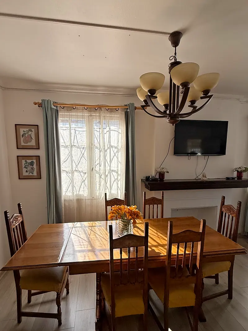 Comedor con mesa de madera, sillas tapizadas en amarillo y una lámpara de techo, con la luz de la ventana sobre la mesa