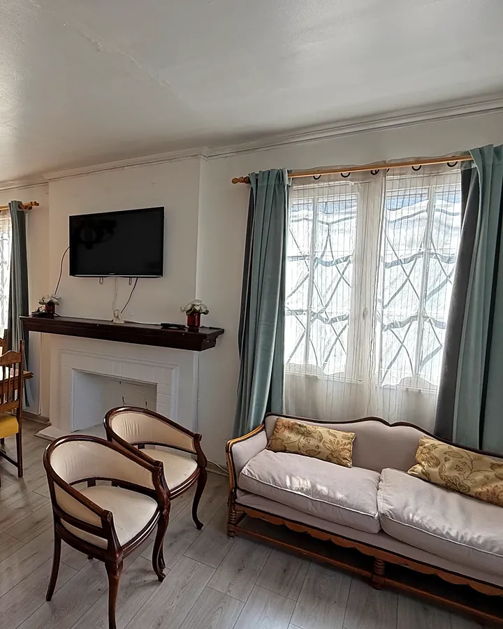 Sala de estar con sofá, sillones, chimenea blanca y cortinas gris azuladas