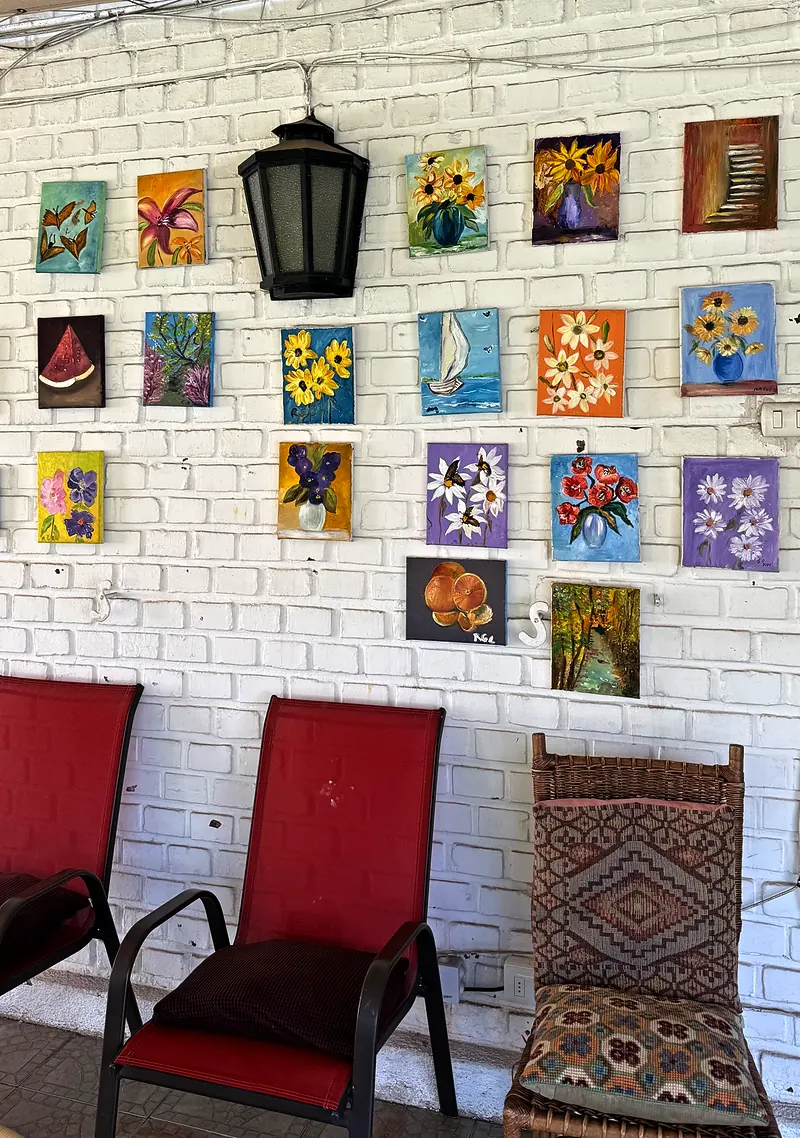 Muro de ladrillo blanco con cuadros de flores pintados en el taller de la casa, junto a una farola y sillas rojas