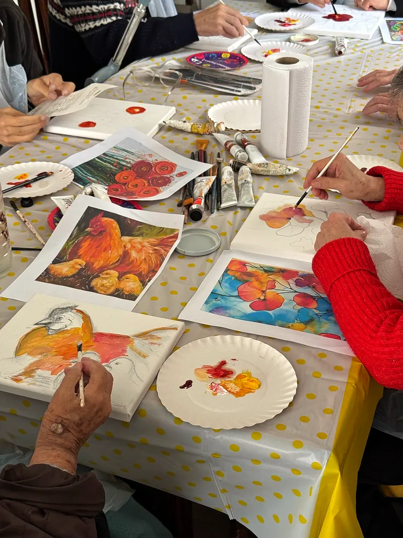 Manos de residentes pintando sobre lienzos con pinceles y paletas de cartón, sobre un mantel de lunares amarillos